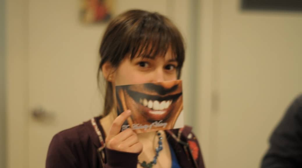 Woman with otherwise serious expression holds a picture of a smile across her mouth